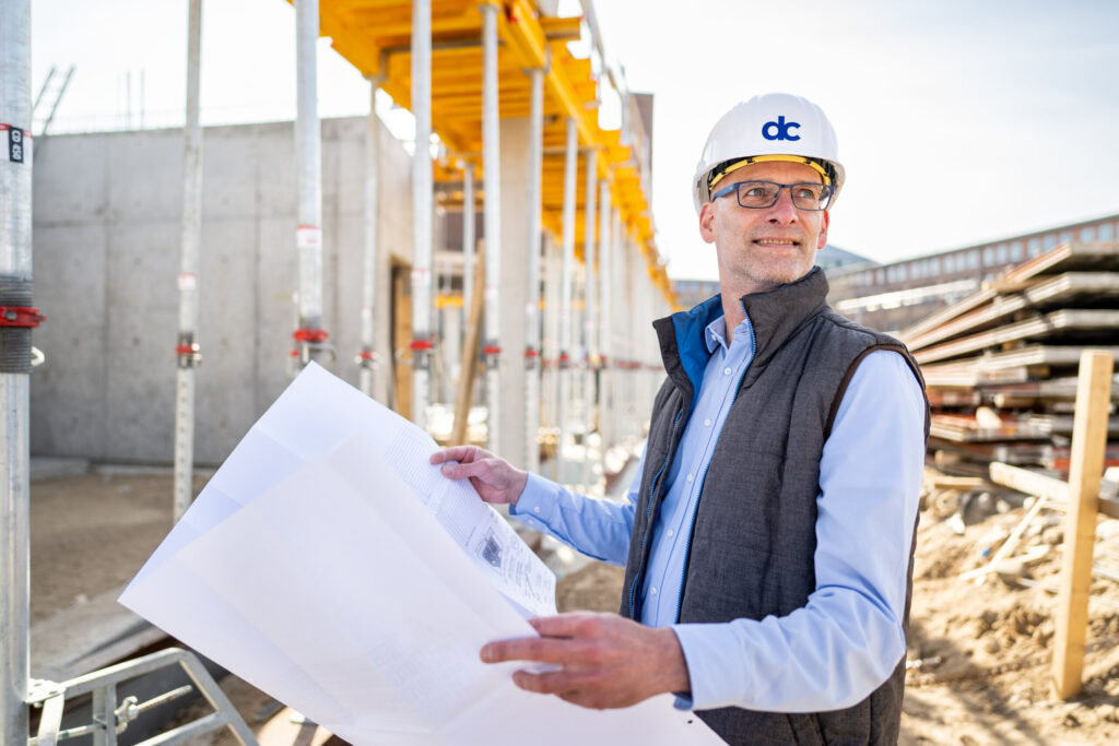 Projektentwickler mit Bauplänen auf einer Baustelle der dc Gruppe