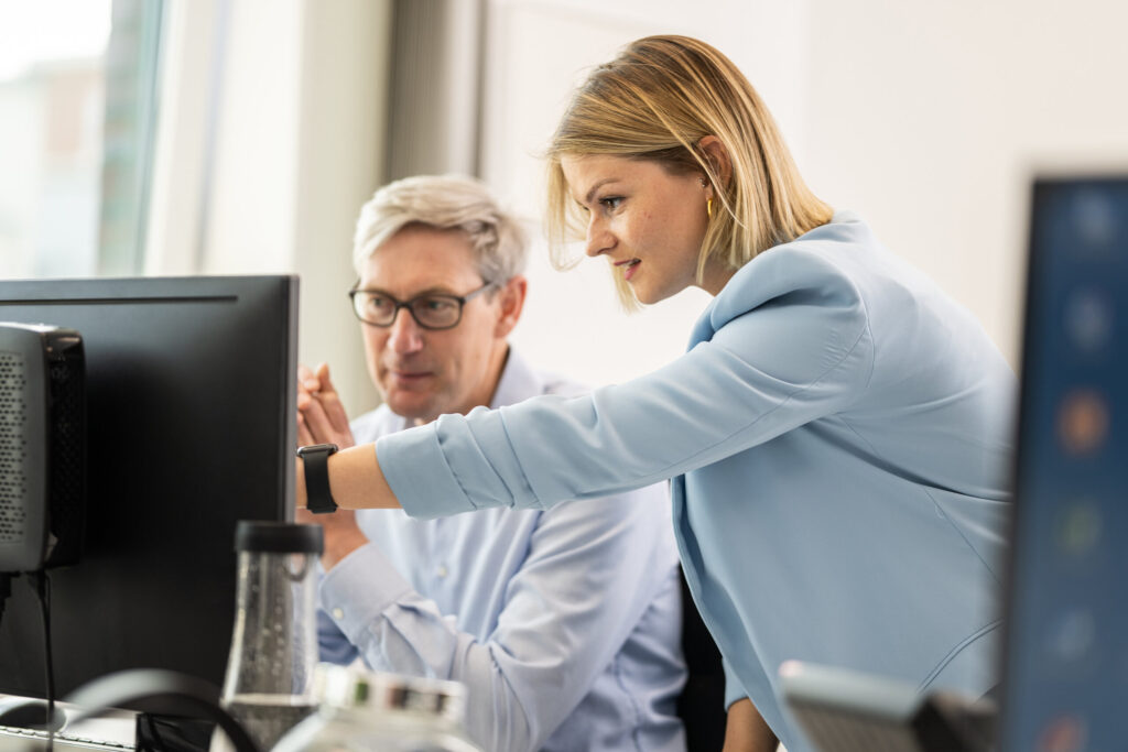 Zwei Kollegen besprechen sich am Bildschirm im Büro